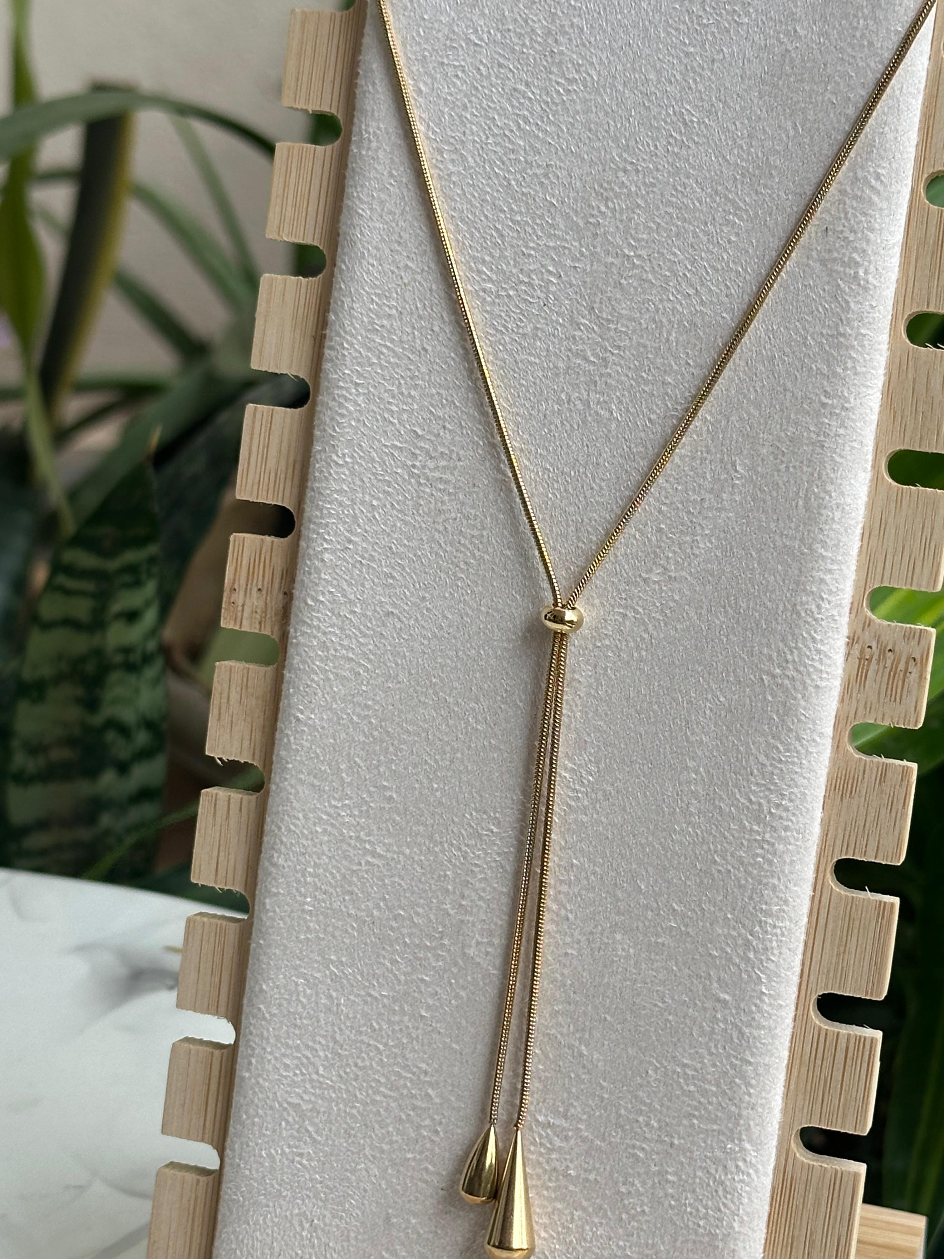 Gold lariat Y-necklace with teardrop tassels on display stand close up