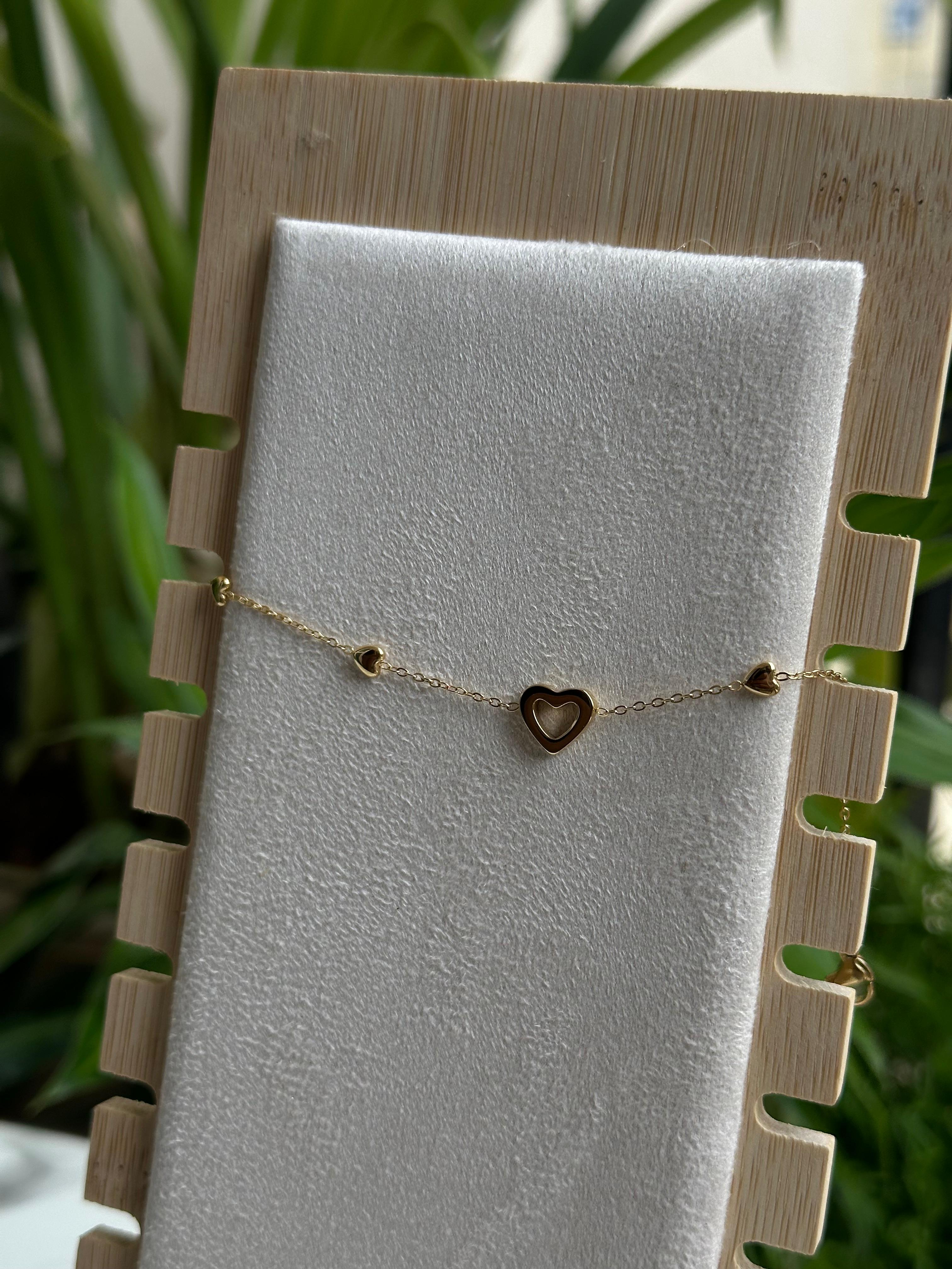 Gold multi-heart charm bracelet on white display stand