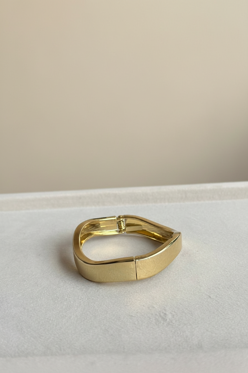 Sculpted gold cuff bracelet photographed on a warm ivory luxury studio background