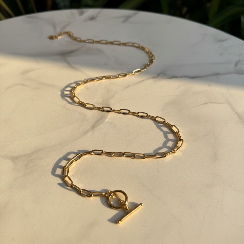 Gold paperclip chain necklace on white marble surface